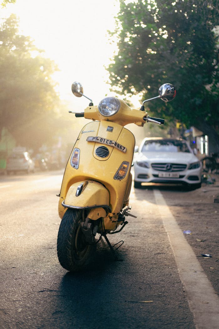 A bright yellow scooter parked on a quiet Indian street in Puducherry during sunrise.