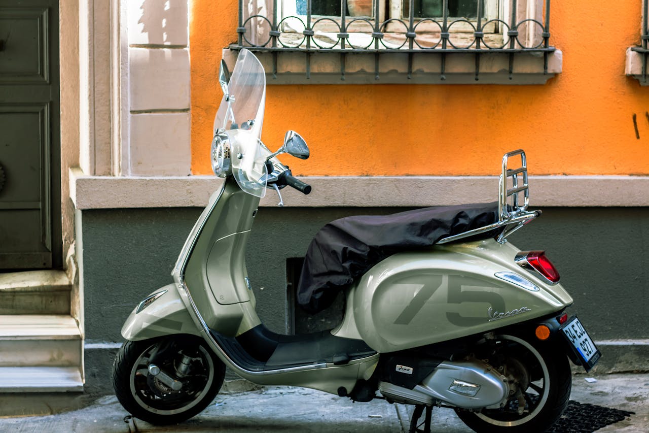 Stylish Vespa scooter parked on a vibrant street with an orange wall. Urban lifestyle imagery.
