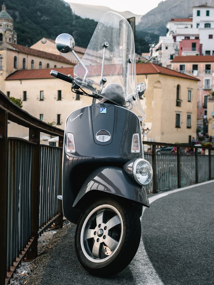 A vintage Vespa scooter parked on a winding street in a picturesque urban setting with historic buildings.