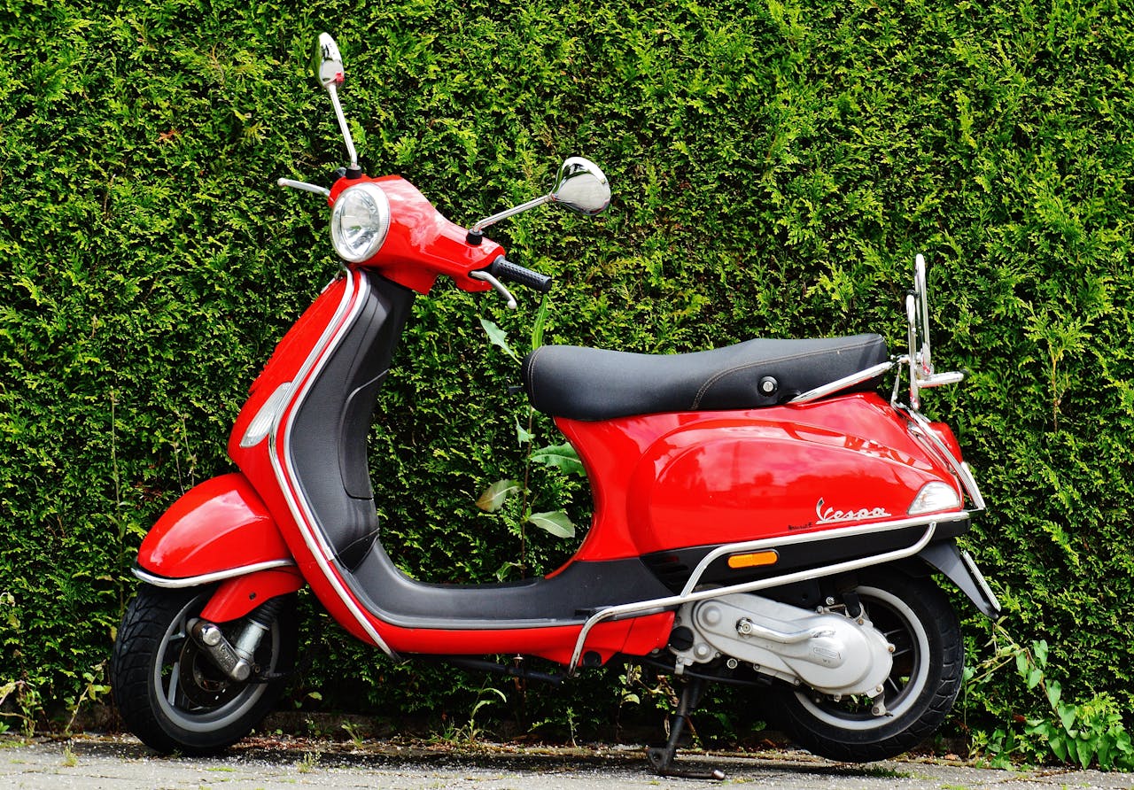 Bright red Vespa scooter parked against a lush green hedge, showcasing vibrant contrast.