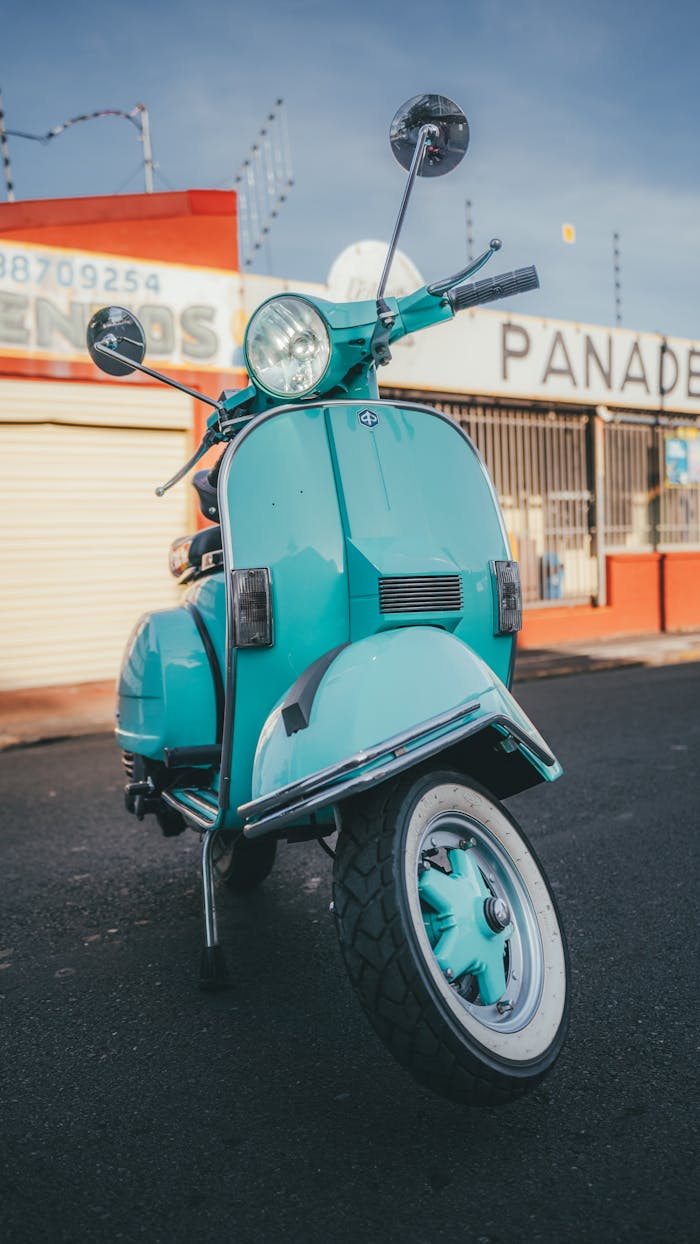 Close-up of a classic turquoise Vespa parked on an empty urban street.